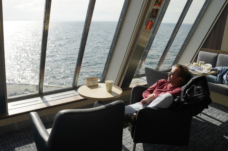Man sitting in the sun on a ferry deck in a luxury chair with the ship’s bow in view