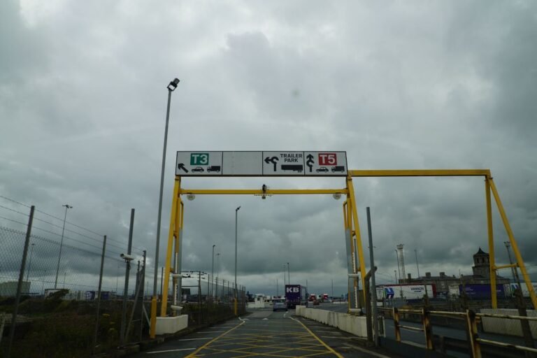 Gray, cloudy sky with a yellow structure above the road displaying signs for cars and trucks.